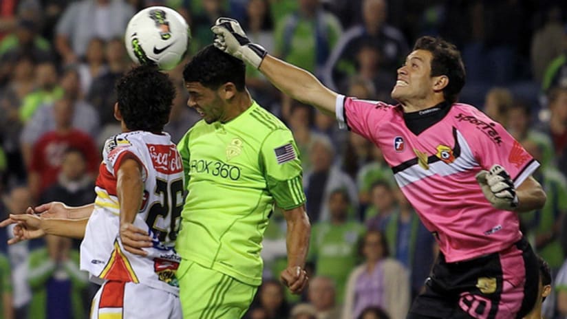 Herediano goalie Daniel Cambronero punches the ball away before Seattle's Lamar Neagle can get to it.