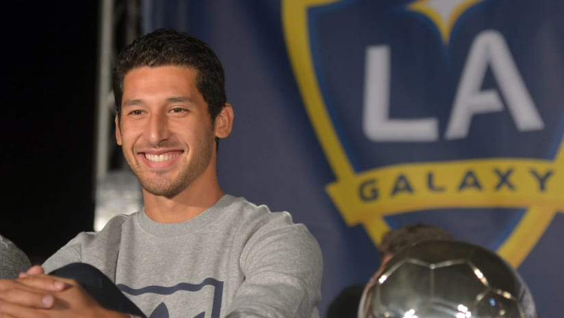 Omar Gonzalez, smiling in street clothes with a trophy
